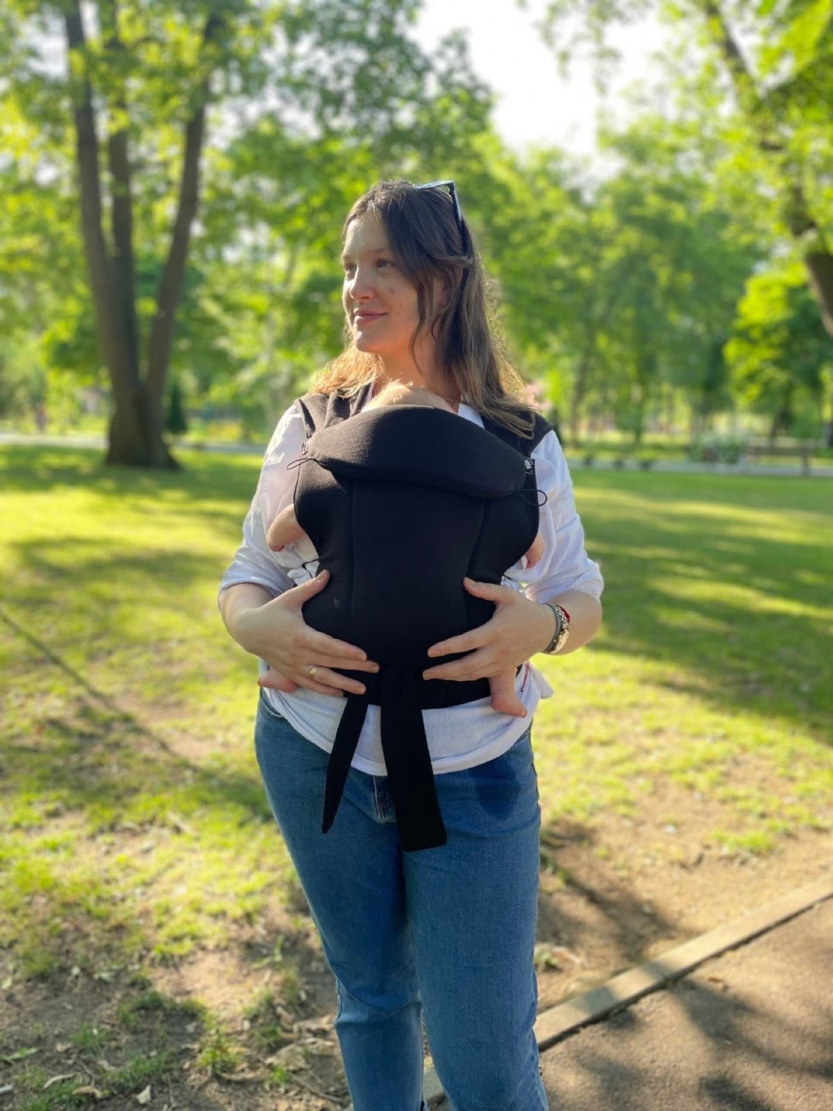 Părinte purtându-și copilul aproape, într-un marsupiu Baby Hug